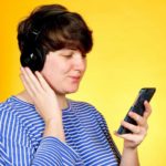 Image of a woman wearing headphones and listening to a smart phone.
