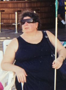 Photo of Bernice Kandarian. She has dark hair, is wearing sunglasses and holding her white cane.