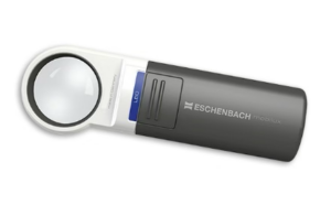 A handheld magnifying glass with a built-in LED light. It has a white circular lens area and a dark gray handle. The brand name "Eschenbach Moblilux" is printed on the handle, and there's a blue button marked "LED" for activating the light. The design is compact and portable.