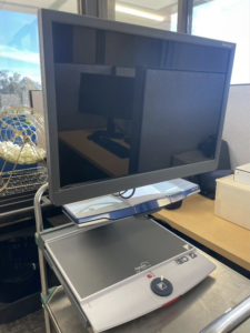 A Clear View+ desktop video magnifier. It has a large screen monitor, an autofocus camera, and a flat platform for placing documents. The monitor is tilted forward.